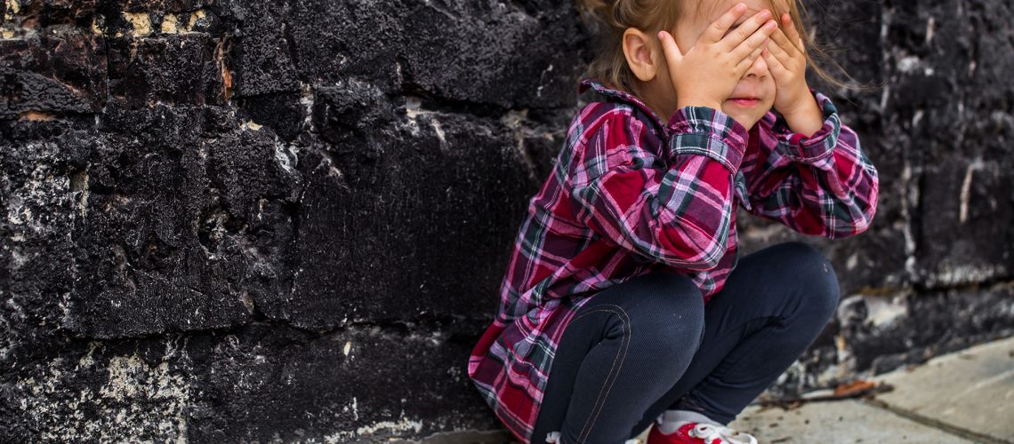 llittle beautiful girl near brick wall with red sneakers and a plaid shirt, emotion girl